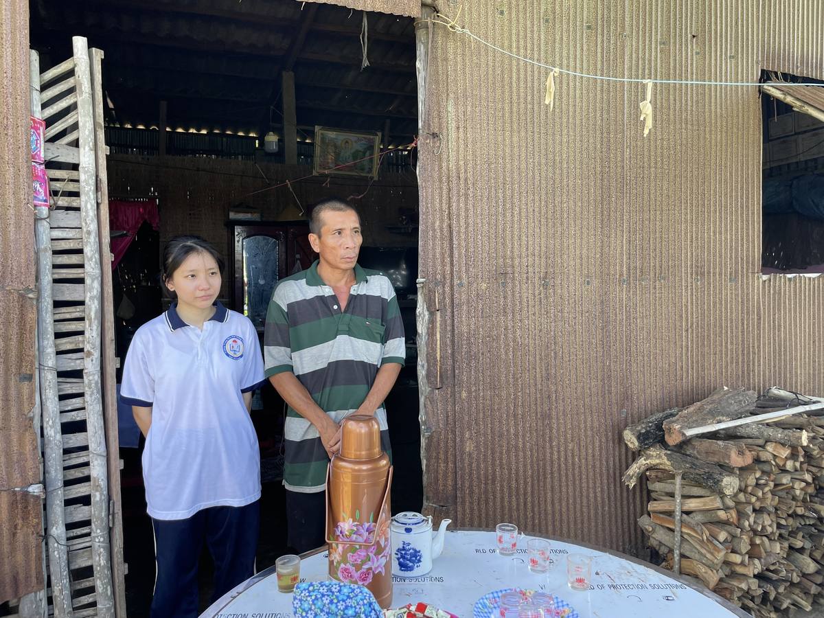 A volunteer standing with a scholarship student's father inside the family home